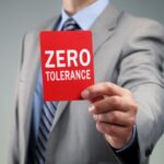 Man holding red poster with 'Zero Tolerance' on it